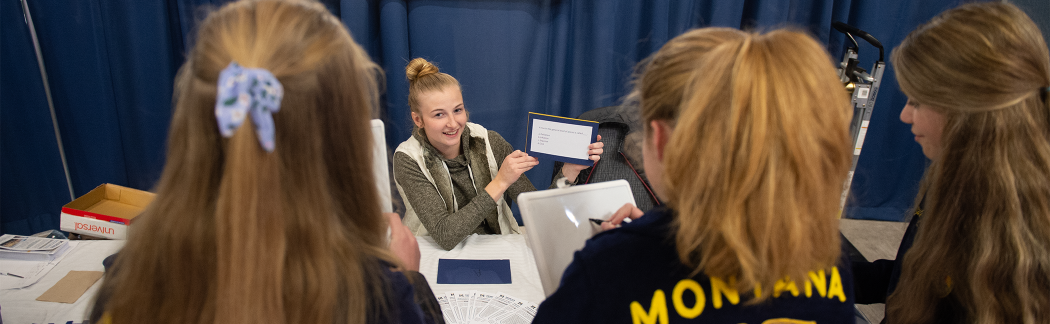 A stuent at a booth talking to three young girls.