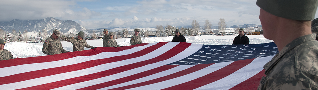 A group of young soldiers in uniform hold the United States flag aloft.