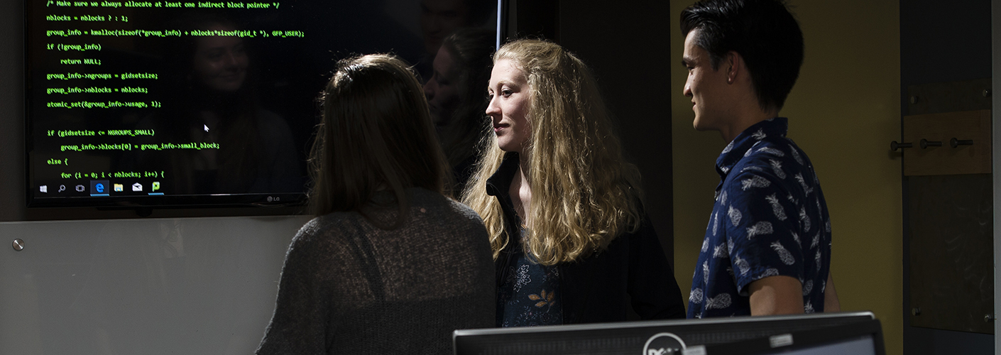 A group of two women and one man consider lines of code on a screen.