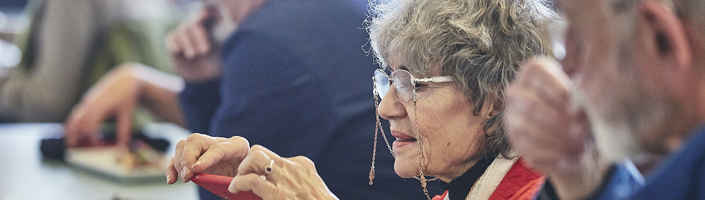 An older woman with reading glasses takes a photograph.