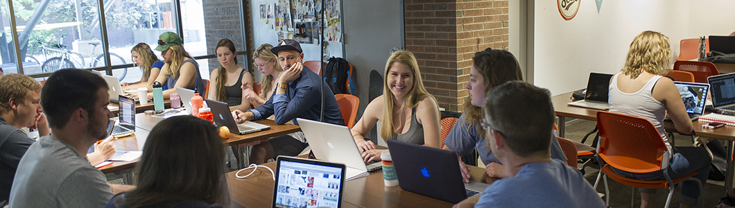 A group of students in a computer lab discuss their work.