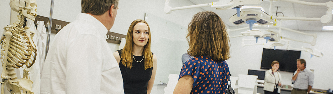 A young woman stands in a health care facility, talking to a man and a woman.