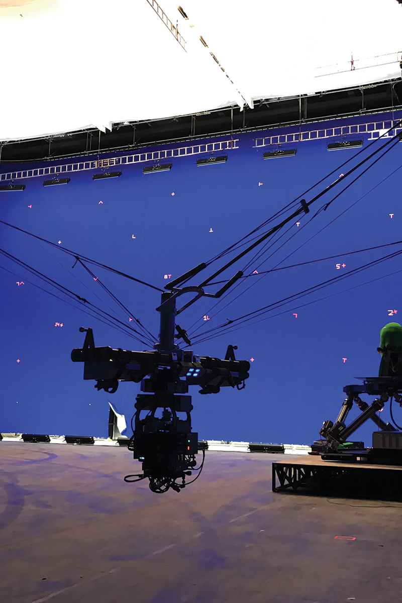 A studio camera pointing at a figure on a small platform with a purple backdrop