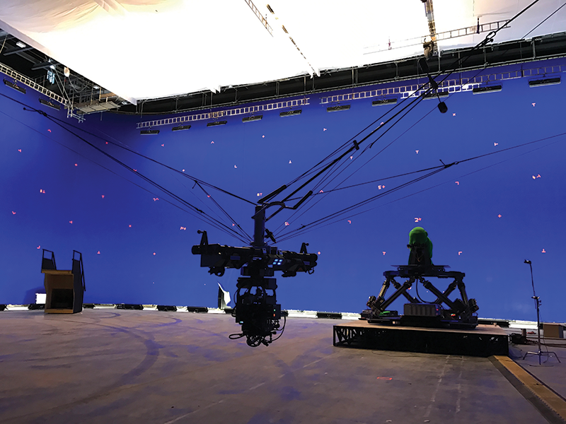 A studio camera pointing at a figure on a small platform with a purple backdrop