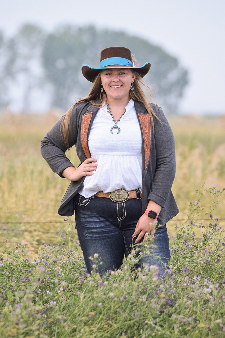 A woman stands for a portrait in a field of purple alfalfa. 