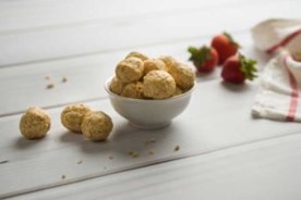 Energy bites in a bowl on a table next to three energy bites and three strawberries.