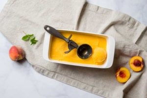 A dish containing peach Fruit Sorbet and an ice cream scoop. 