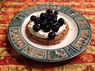 A wheat toaster waffle on a plate topped with yogurt and blueberries.