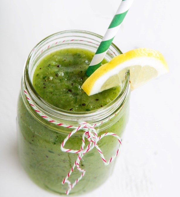 A Mason jar of Groovy Green Smoothie, garnished with a lemon slice and striped straw.