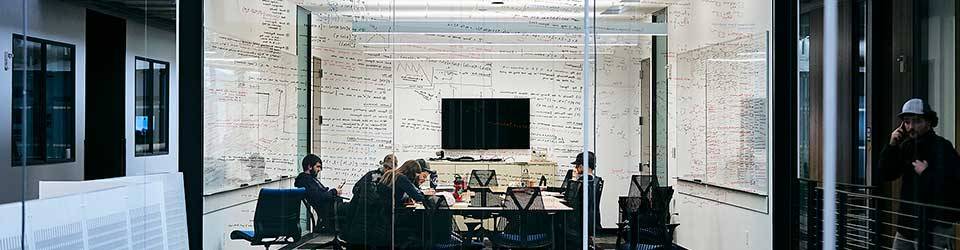 Students in a seminar room with whiteboards and a video screen on the wall