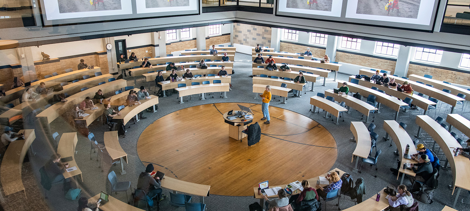 A classroom with rounded tables forming a circle around a central speaker