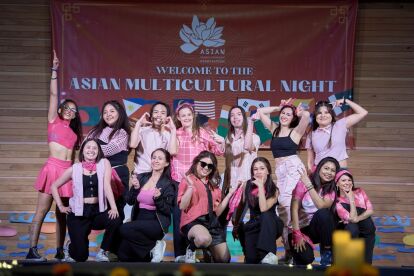 Group of students posing on stage during Asian Multicultural Night event with a banner behind them.