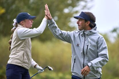 Golfer and coach exchange a high-five during a golf event on a cloudy day.