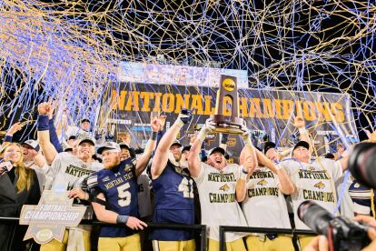 College football team celebrates winning the National Championship, holding the trophy under blue and gold streamers.