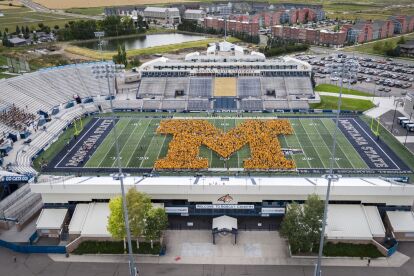 Aerial view of a stadium with people forming a large yellow M on the football field.