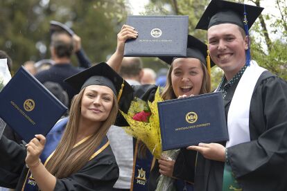 Three graduates in caps and gowns hold up Montana State University diplomas and smile during commencement.