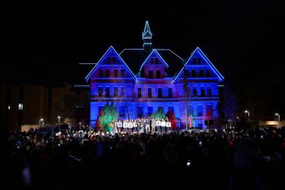 Crowd gathers at night in front of a large historic building lit with blue lights during an outdoor event.