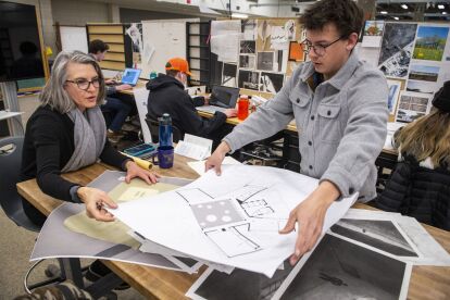 Architecture students and instructor review building plans and design layouts in a studio workspace.