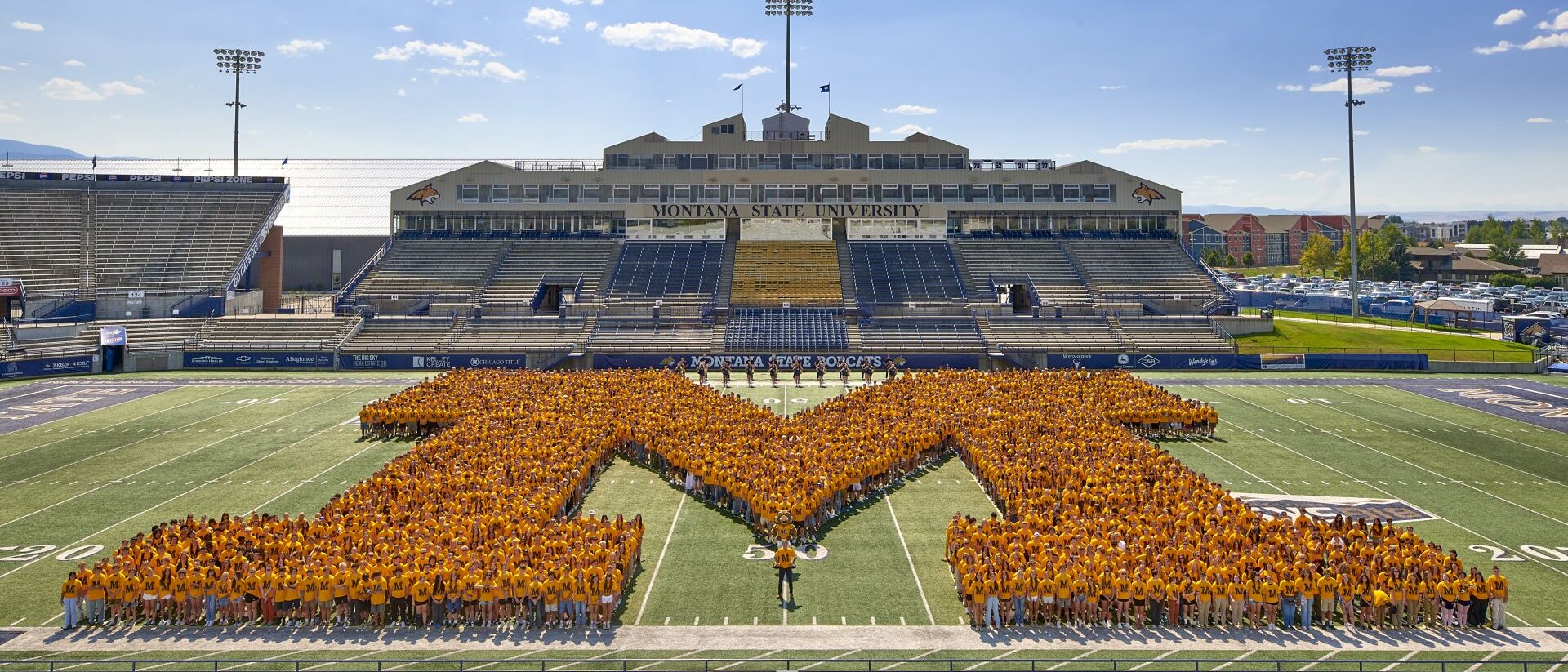 Hundreds of people form a large M shape on the field at Montana State University’s football stadium.