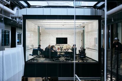 Students collaborate in a glass-walled study room filled with notes and equations on whiteboards.