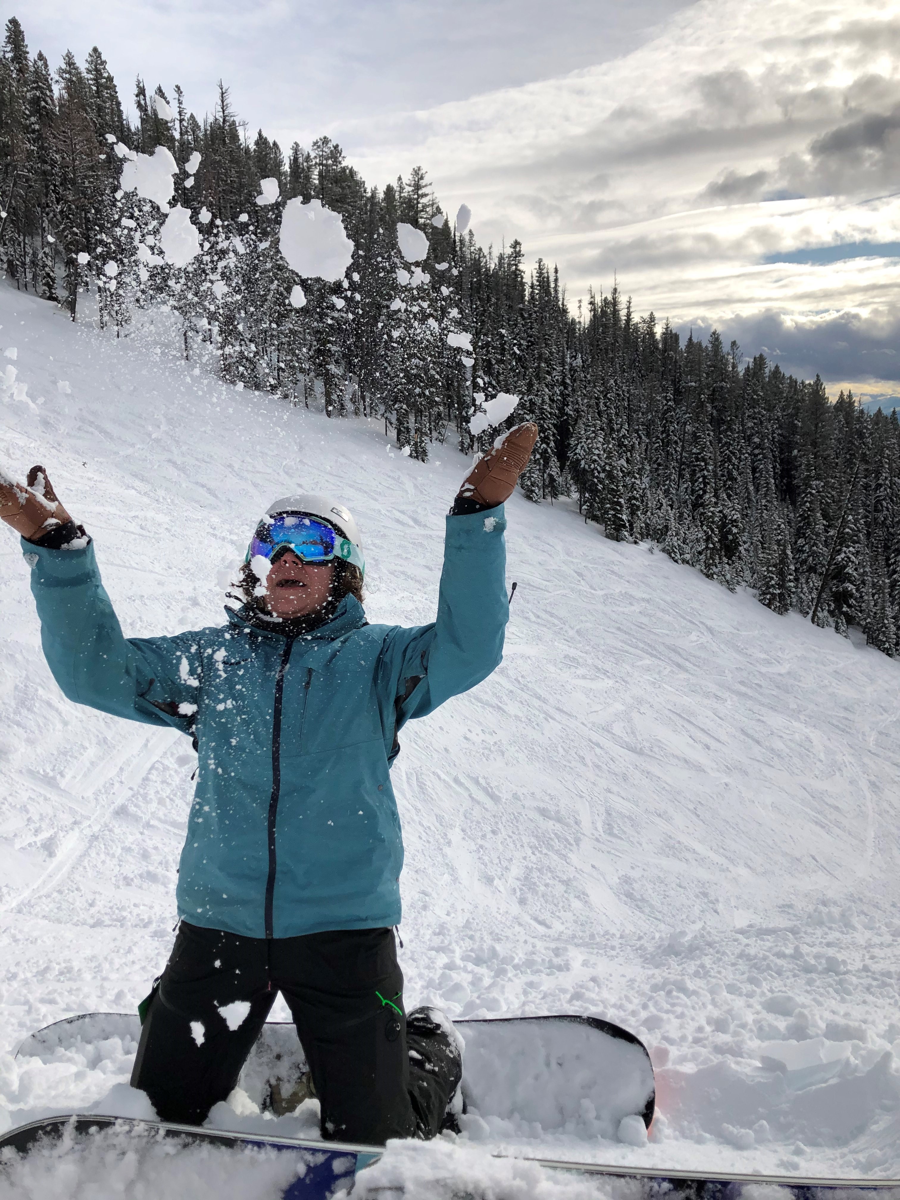 Brook kneeling while snowboarding, throwing snow in the air.