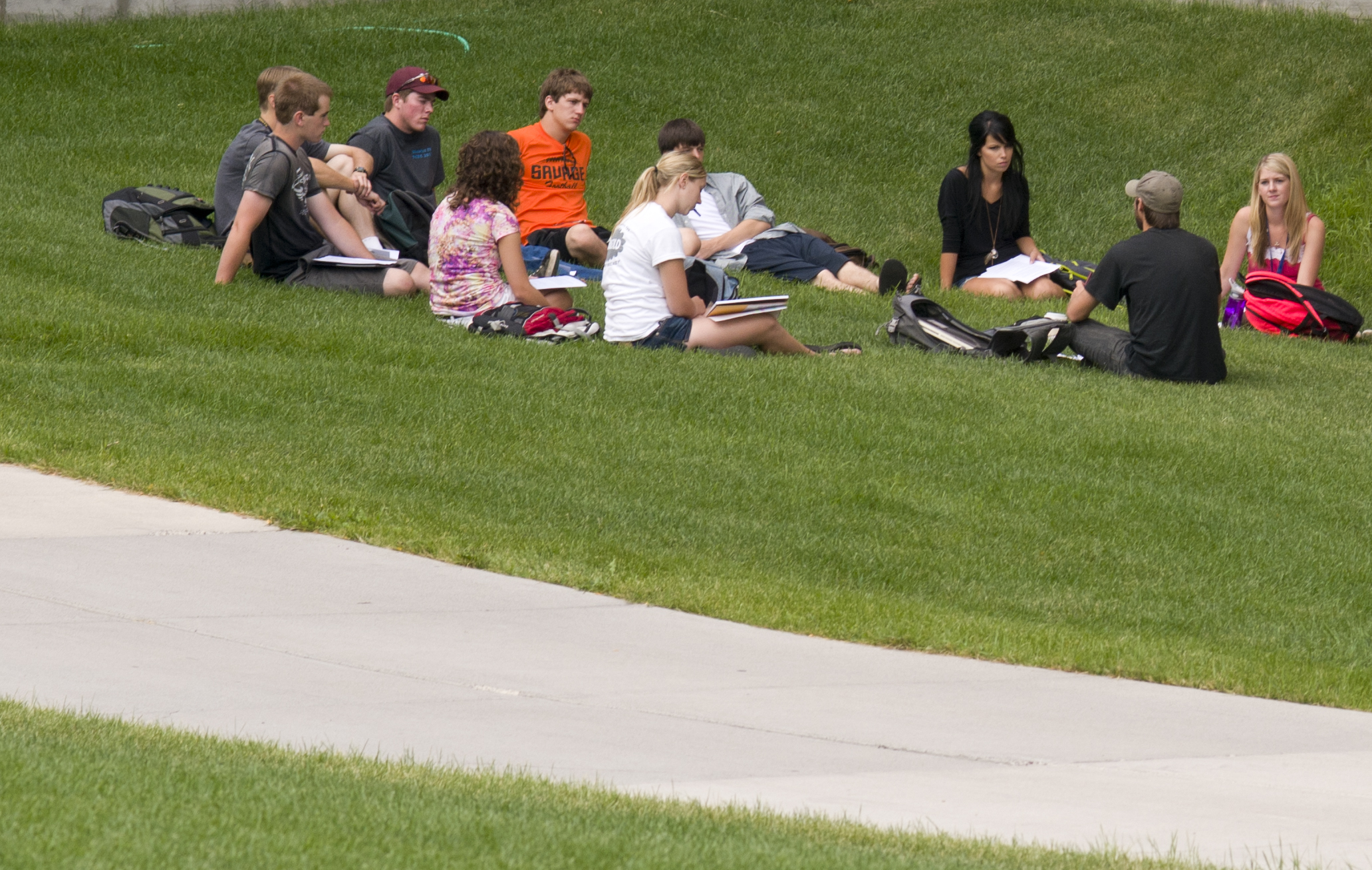 Students sitting in a semicircle on the grass outside talking
